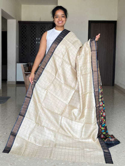Woman holding a cream saree with a black border in an indoor setting