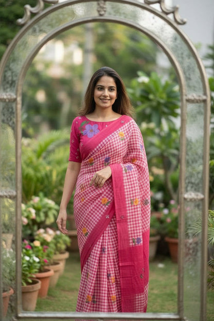 Woman taking a mirror selfie wearing a pink saree with floral patterns.