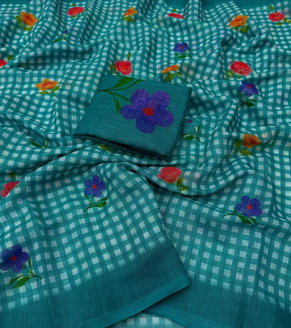 A teal and white gingham check saree with scattered embroidered floral motifs in purple, red, and orange, featuring a matching folded fabric piece with a large purple flower design.