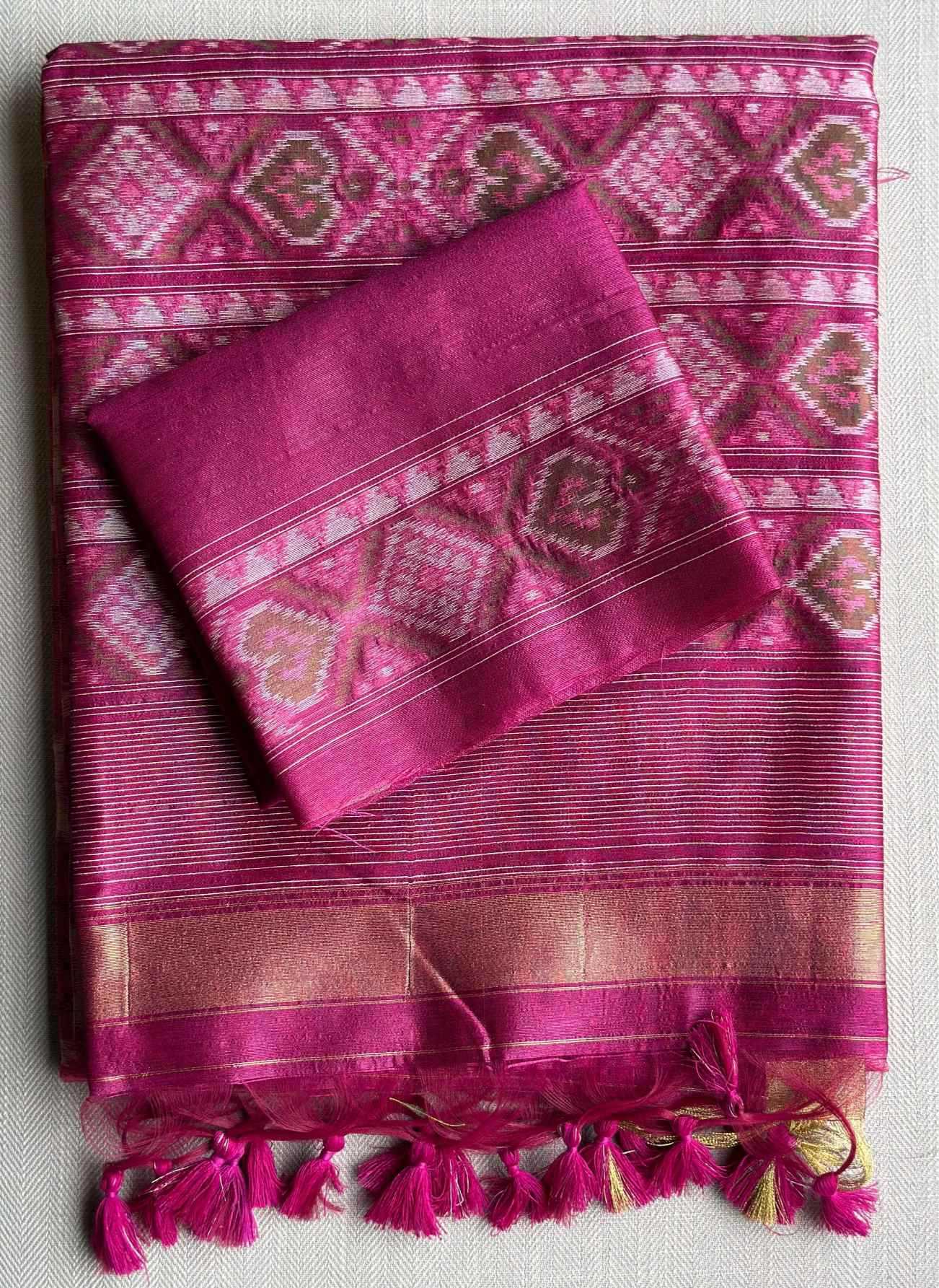 A folded magenta pink silk saree with intricate geometric and floral patterns in pink, white, and gold, featuring matching tassels at the bottom.