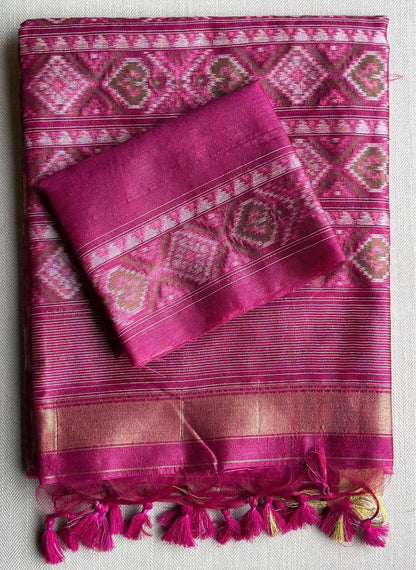 A folded magenta pink silk saree with intricate geometric and floral patterns in pink, white, and gold, featuring matching tassels at the bottom.