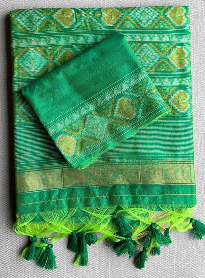 A green patterned textile, likely a sari or scarf, laid flat on a light gray textured background. The fabric features intricate geometric and floral motifs in lime green and yellow-green, with a striped border and matching tassels along the bottom edge.