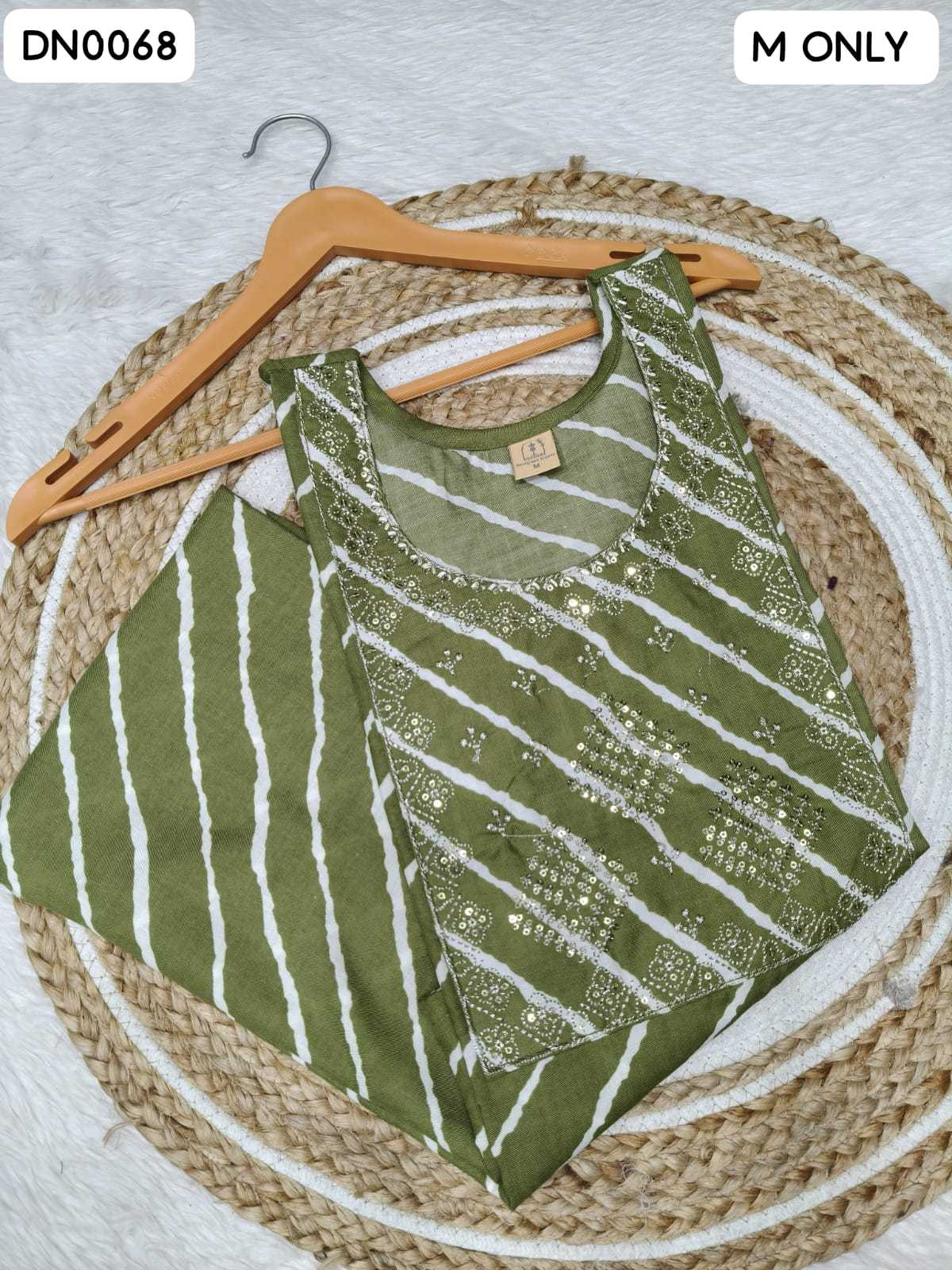 An olive green sleeveless top with white vertical stripes and silver sequin embellishments, displayed on a wooden hanger over a woven round mat.