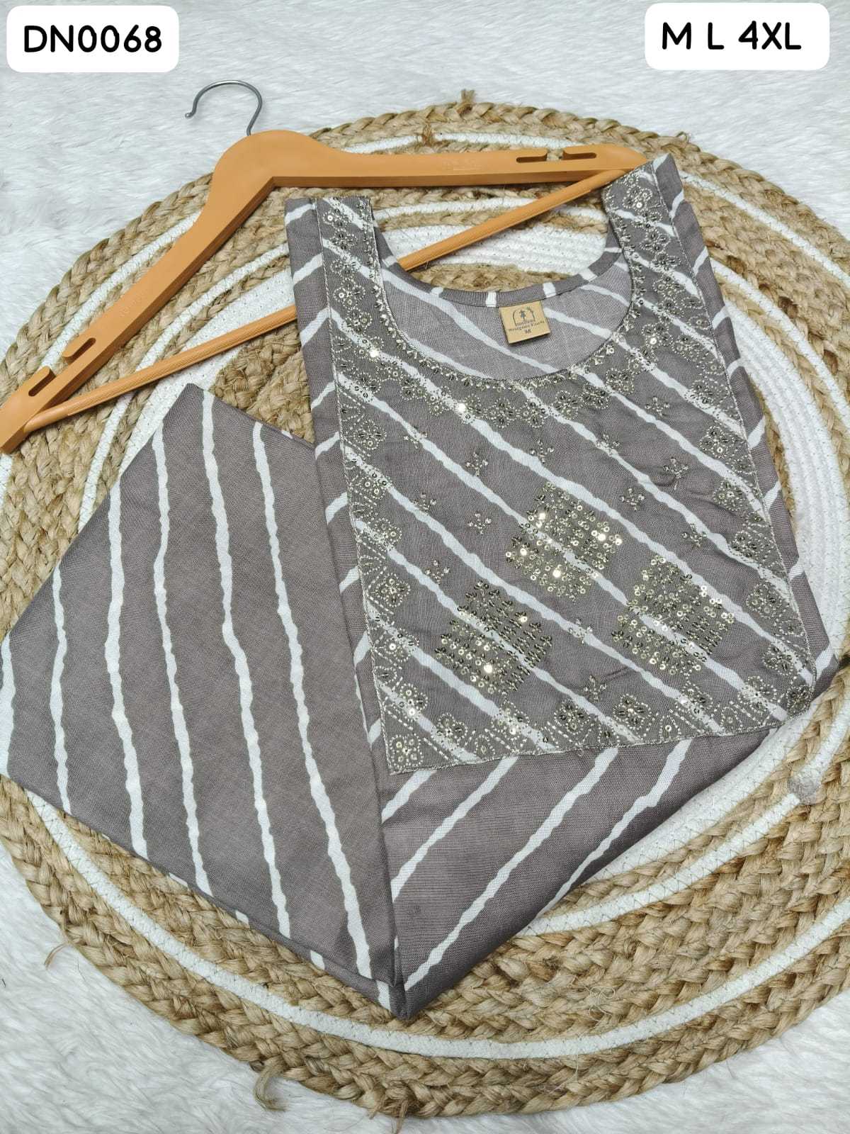 A folded women's kurta set in taupe gray and white, featuring vertical stripes on the body and white stripes with metallic gold embroidery on the yoke. The kurta is displayed on a wooden hanger over a round woven jute mat on a white textured background.