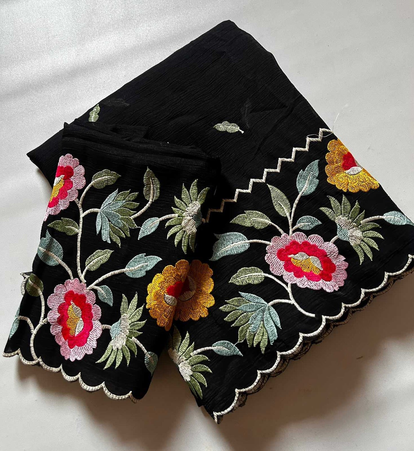 Black fabric with colorful floral embroidery on a white background