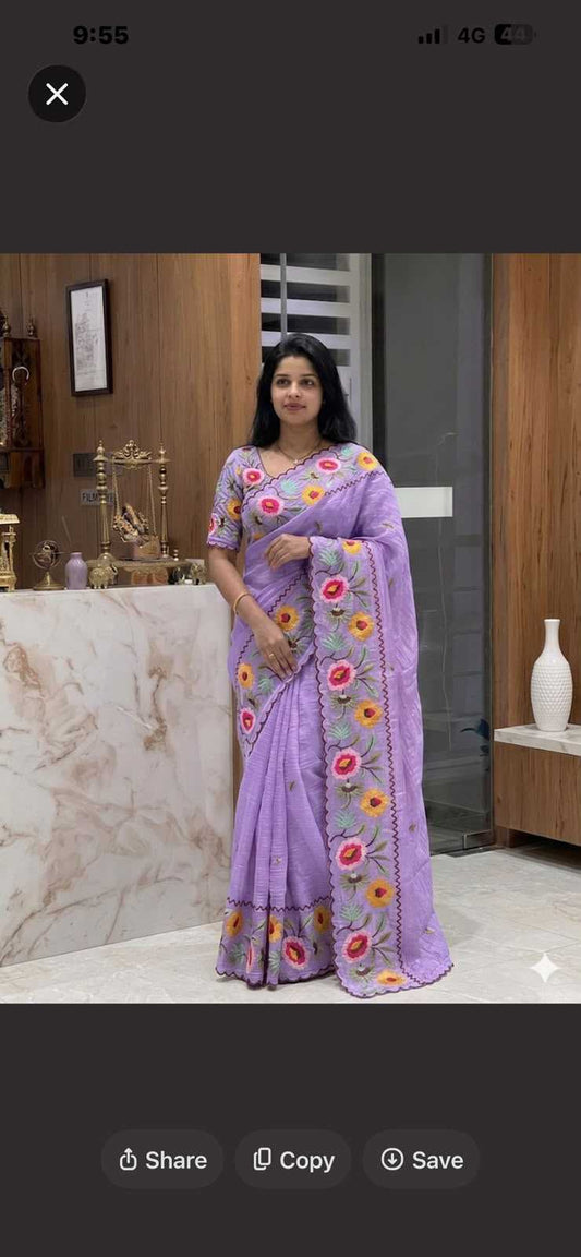 A woman wearing a lavender purple saree with colorful floral embroidery, standing in an indoor setting with a marble counter and wooden wall in the background.