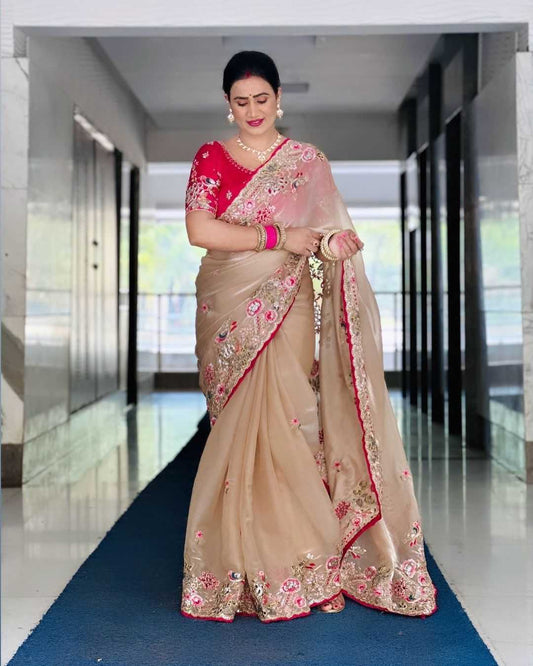 Woman wearing a beige saree with pink floral patterns in an indoor setting