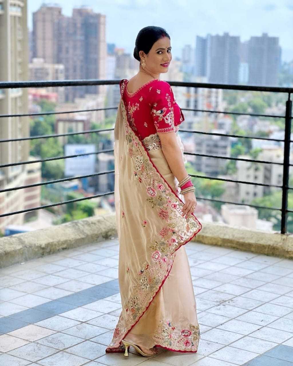 Woman in a saree standing on a balcony with a cityscape view