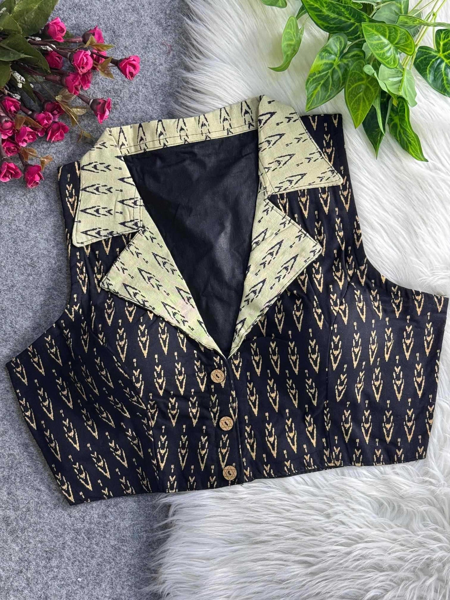 Black patterned vest with cream collar on a textured surface with flowers and leaves.