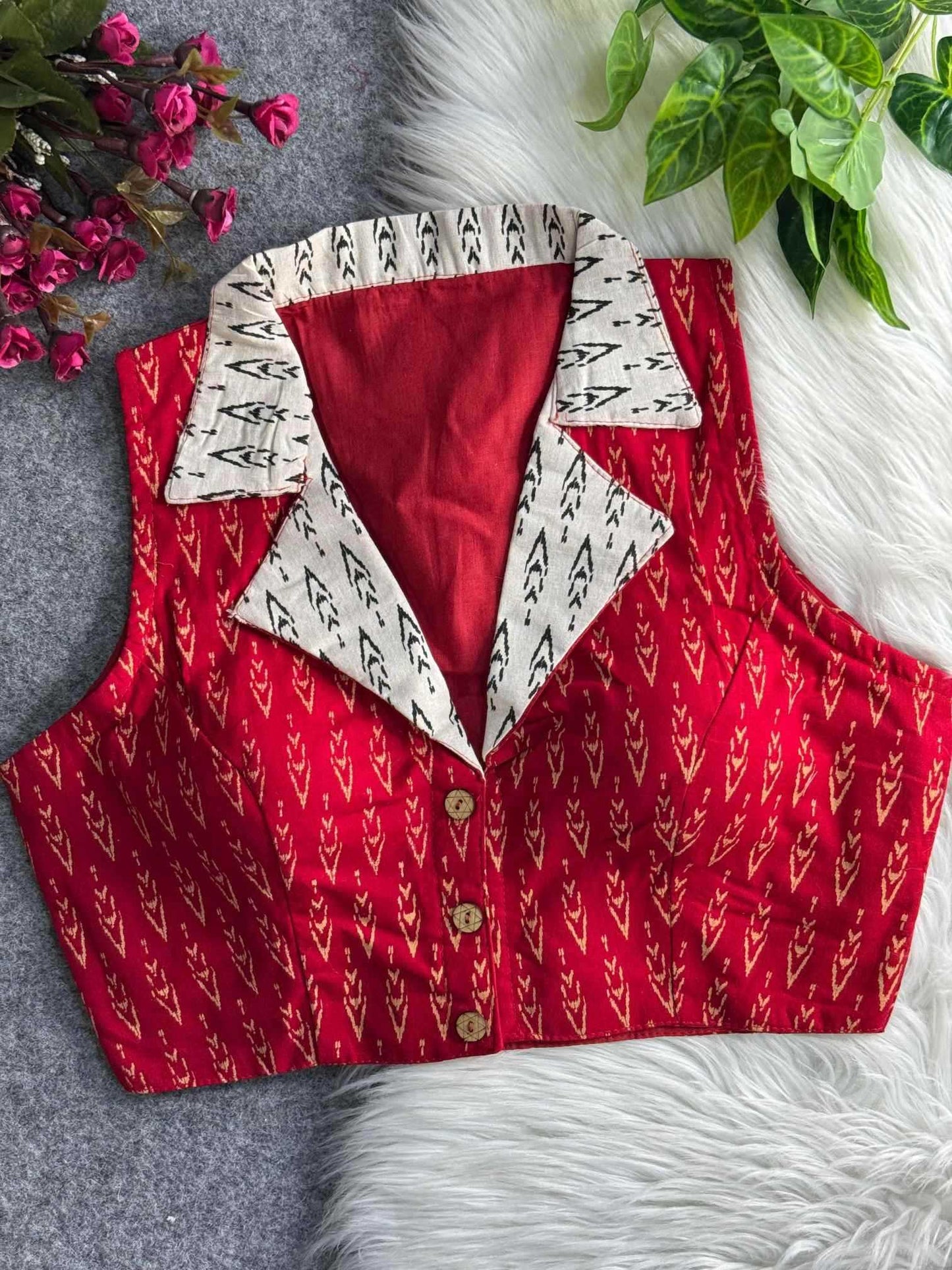 Red patterned vest with white collar on a textured surface with flowers and leaves.