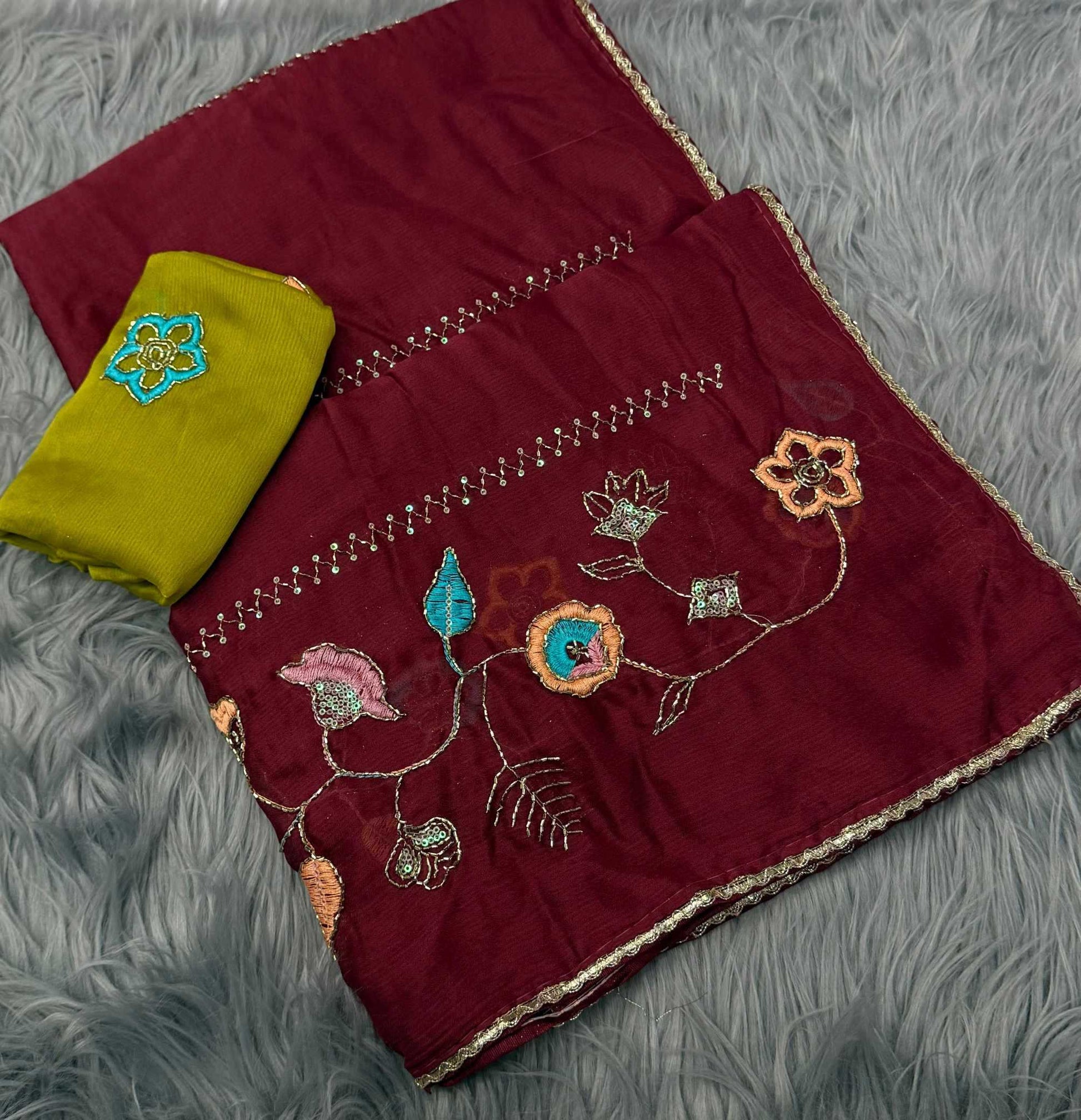 A folded deep maroon fabric set with colorful floral embroidery and a contrasting olive green fabric piece, displayed on a gray faux fur background.