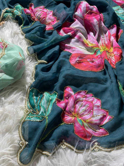 A dark teal blue sheer scarf with large pink and red floral prints and gold embroidered borders, draped on a white faux fur surface next to a mint green matching fabric piece.