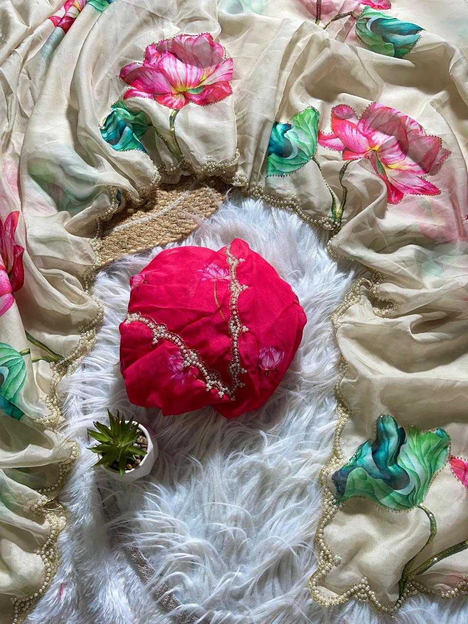 A beige printed scarf with pink and green floral motifs and gold border trim, arranged on a white faux fur surface with a bright pink wrapped headwrap and a small potted succulent.