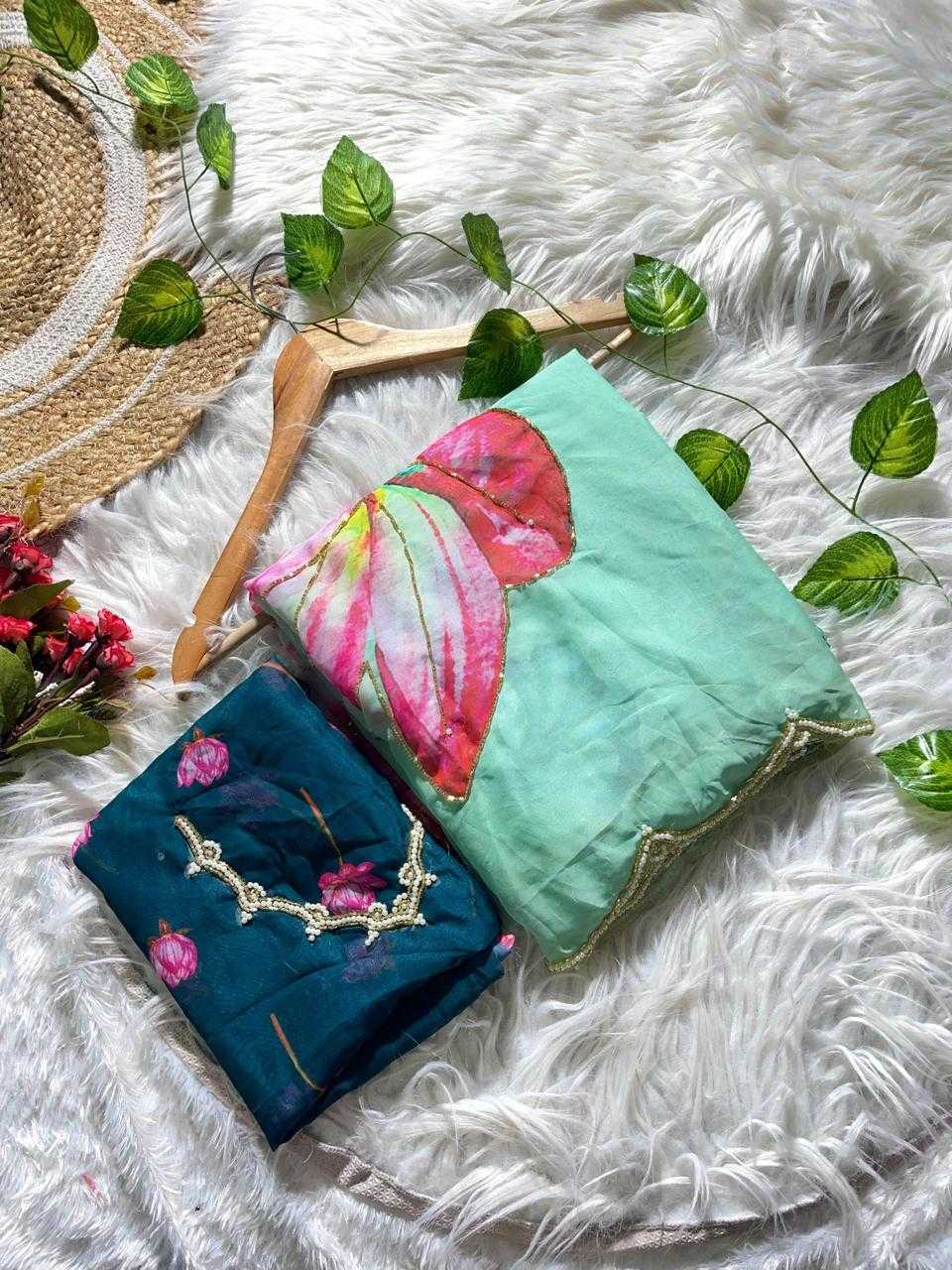 Two folded fabric pieces displayed on a white faux-fur surface with decorative green leaves and a straw hat. One piece is mint green with a large pink and red butterfly motif and gold trim, and the other is dark teal with pink floral embroidery and gold detailing.