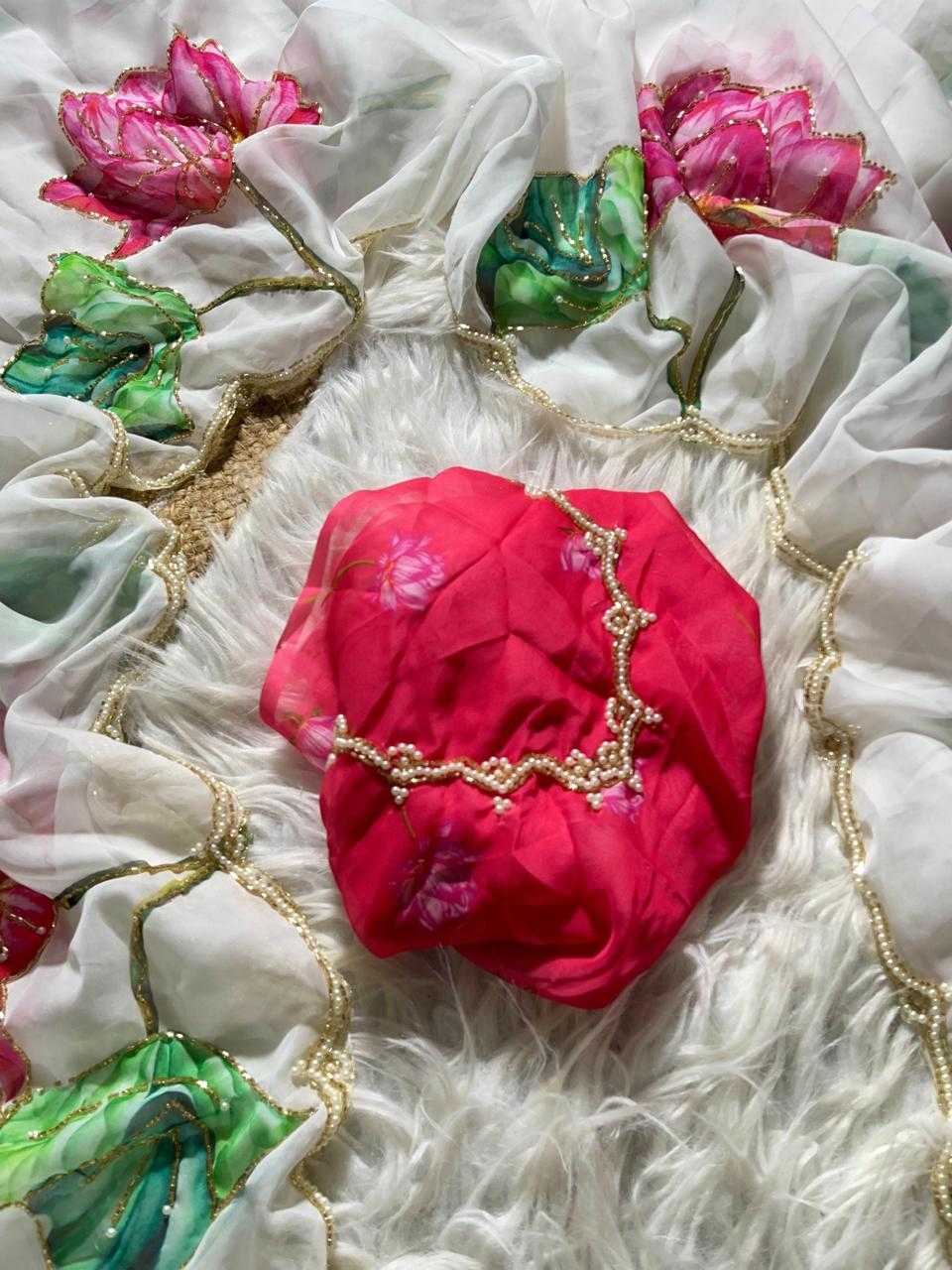 A bright pink fabric accessory, possibly a headwrap or decorative fabric piece, laid on a white faux fur surface surrounded by white sheer fabric with gold trim and colorful floral embellishments.