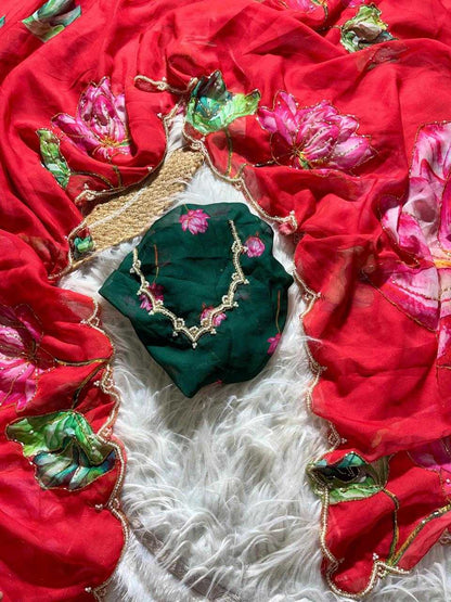 A red embroidered dupatta or scarf with pink floral motifs and gold border details, laid out on a white faux fur surface alongside a dark green blouse piece with pink floral embroidery and a gold necklace.