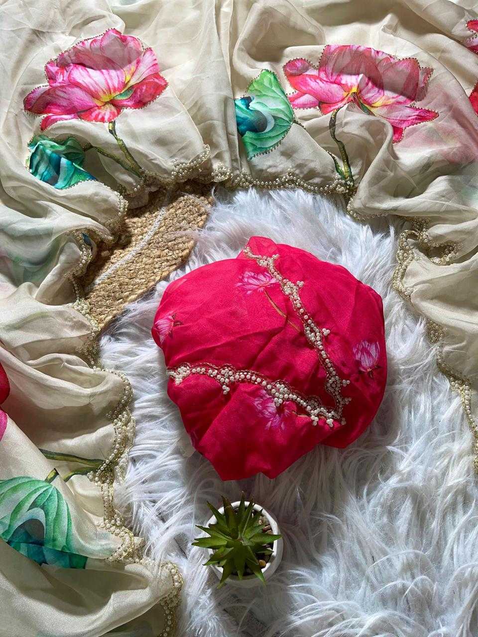 A bright pink fabric headscarf with gold bead embellishments, styled on a white faux fur rug alongside a beige floral printed dupatta and a small potted succulent.