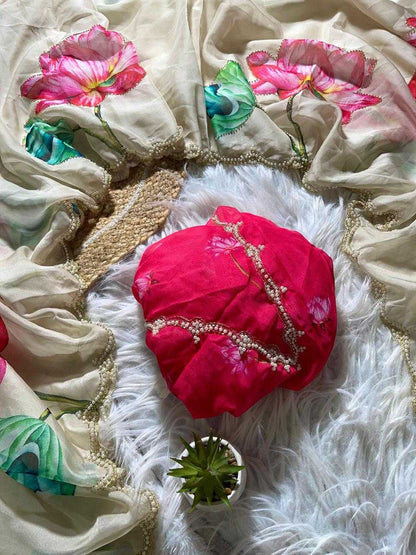 A bright pink fabric headscarf with gold bead embellishments, styled on a white faux fur rug alongside a beige floral printed dupatta and a small potted succulent.