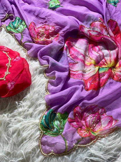 A draped purple fabric accessory with large pink and red floral prints, green leaf motifs, and gold embroidered borders, shown on a white textured rug alongside a red matching piece.