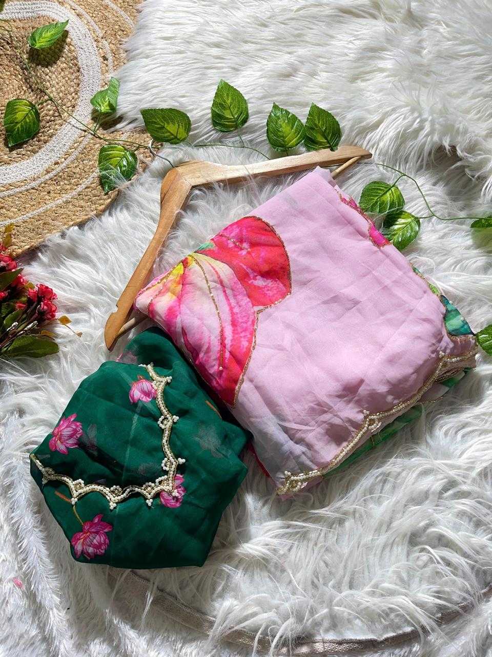 Two folded fabric items, likely scarves or small bags, displayed on a white faux-fur surface with decorative leaves and a woven mat. One item is dark green with pink floral print and gold embroidery, and the other is light pink with a large red floral print and gold trim.