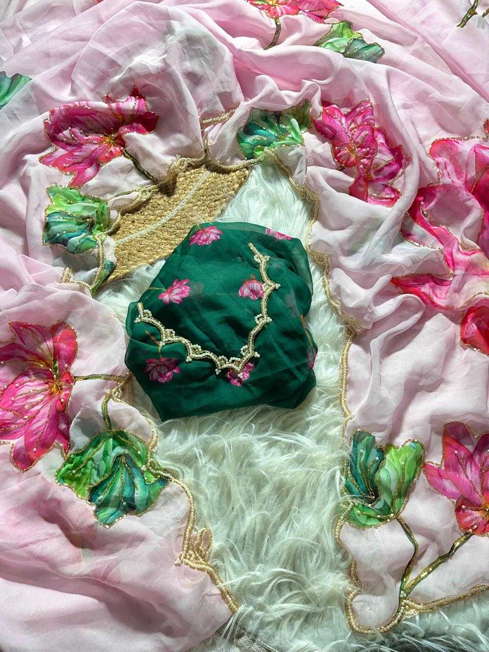 A folded dark green fabric piece with pink floral embroidery and gold trim, placed on a light pink floral dupatta with a white faux fur surface underneath.