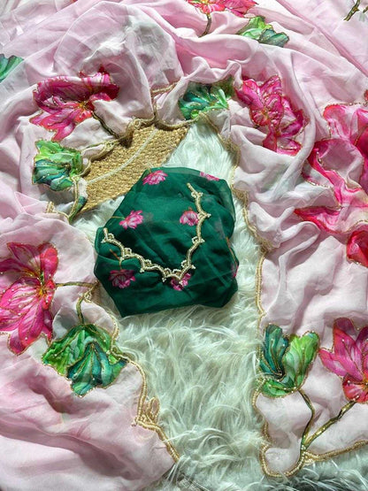 A folded dark green fabric piece with pink floral embroidery and gold trim, placed on a light pink floral dupatta with a white faux fur surface underneath.