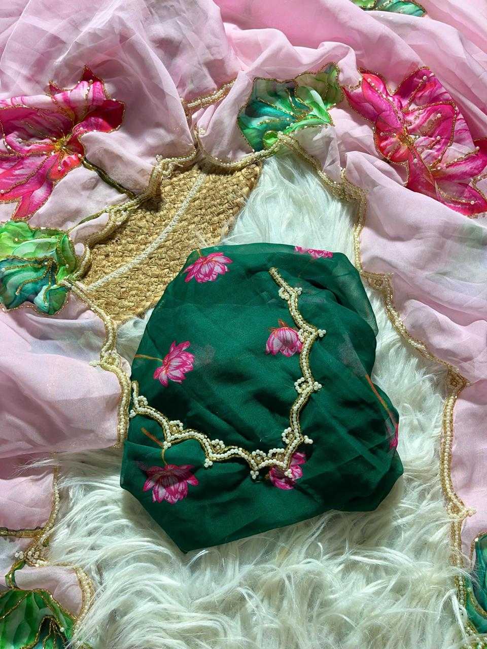 A folded dark green fabric piece with pink floral embroidery and gold trim, placed on a white faux-fur surface with pink and green patterned fabric around it.