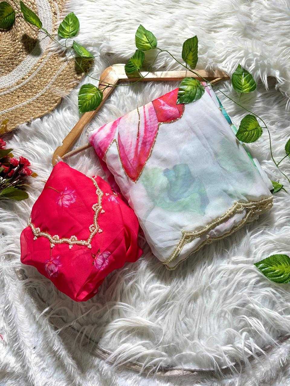 Two folded pieces of fabric or scarf material displayed on a white faux-fur surface with decorative green leaves and a straw hat. One piece is bright pink with gold trim, and the other is white with pink and green floral print and gold trim.