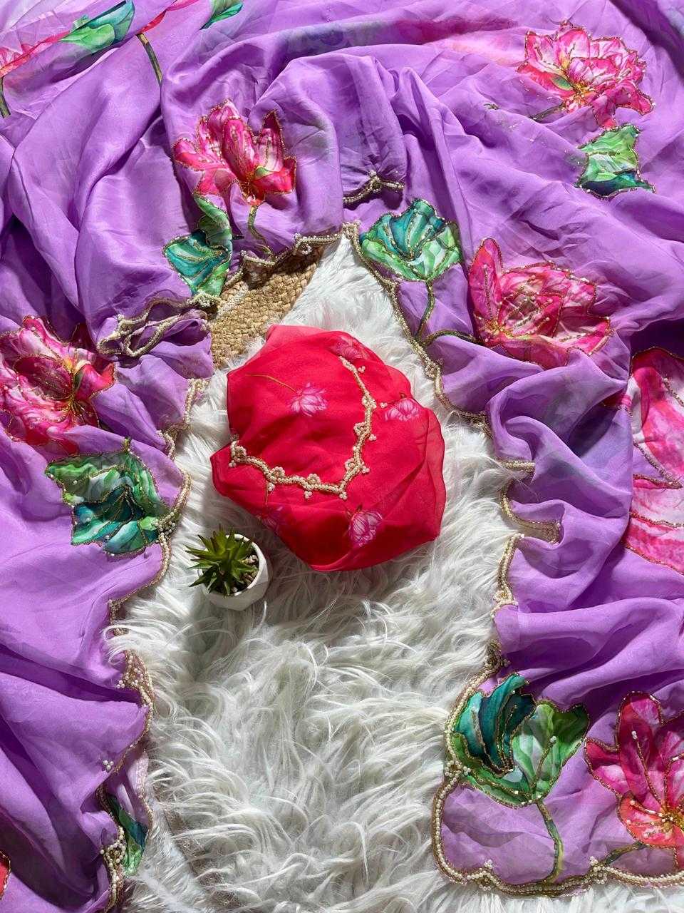 A purple embroidered dupatta or scarf laid out on a white faux-fur surface, featuring pink floral motifs and green leaf embroidery with gold borders. A bright red fabric pouch with gold trim rests in the center, alongside a small succulent.