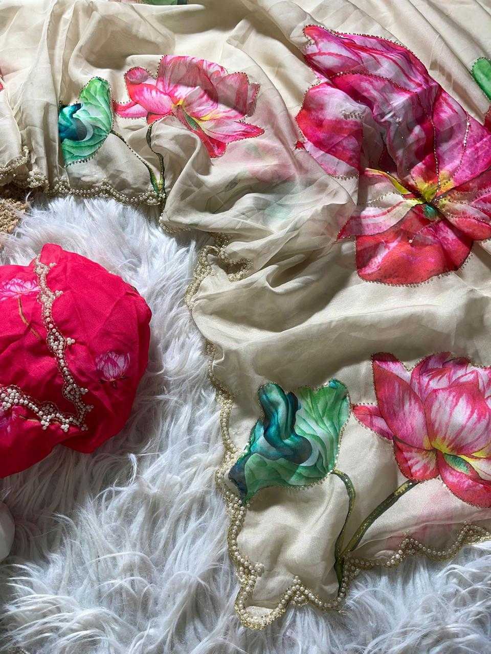 A beige silk-like scarf or dupatta with large pink and red floral prints, green leaves, and gold embroidered scalloped borders, draped over a white faux fur surface alongside a bright pink fabric accessory.