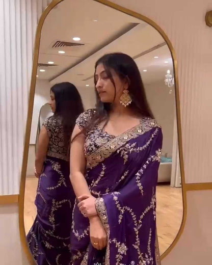 Woman in a purple saree with gold details standing in front of a mirror.