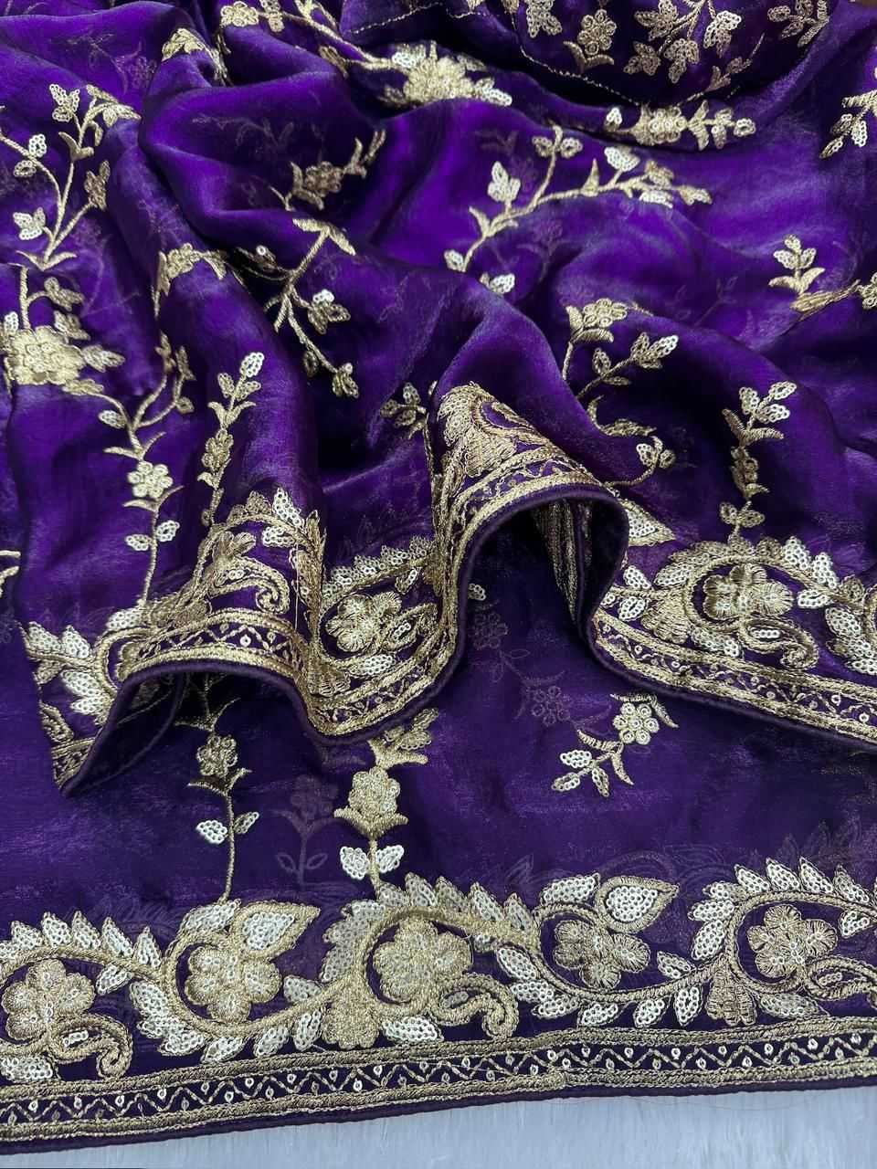 A close-up of a deep purple fabric with intricate gold floral embroidery and a decorative gold border.