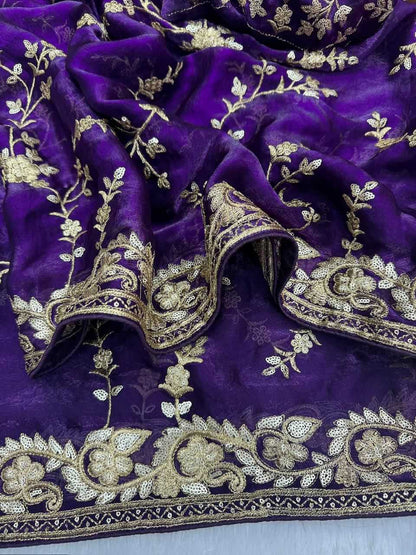 A close-up of a deep purple fabric with intricate gold floral embroidery and a decorative gold border.