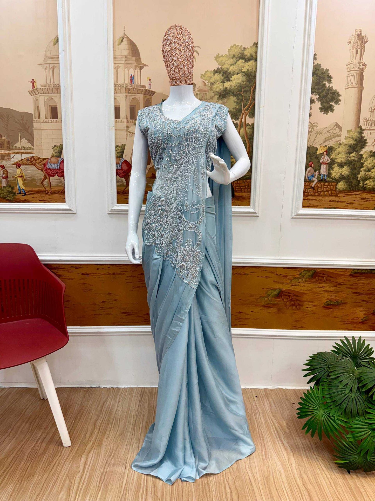 Mannequin wearing a light blue saree with intricate lace detailing in a room with decorative wall art.