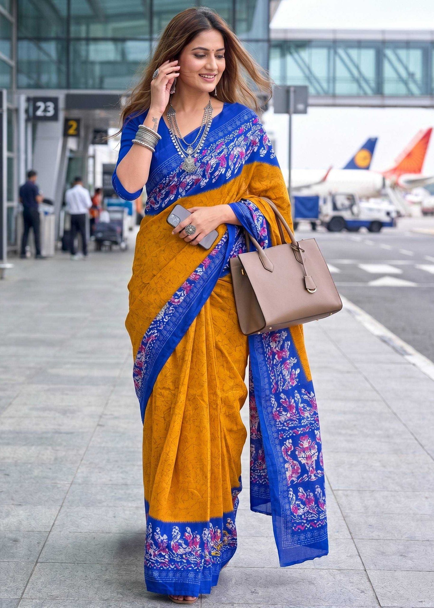Woman in a yellow and blue saree standing near an airport terminal.