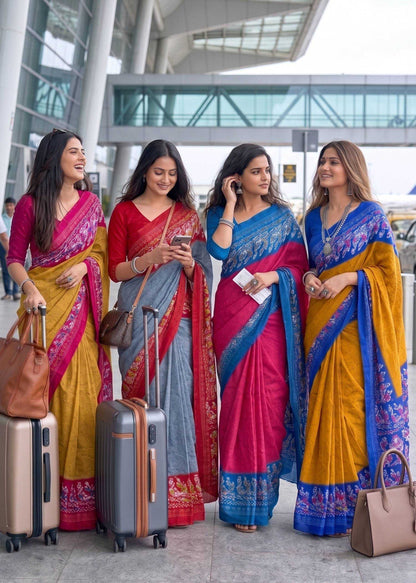 Four women in colorful sarees with luggage at an airport.