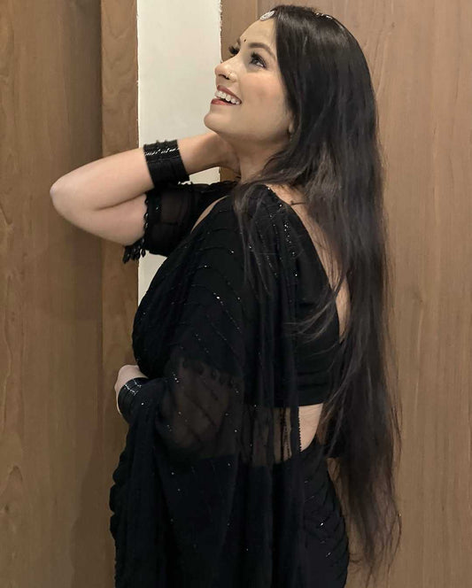 Woman in a black saree with sheer sleeves against a wooden background