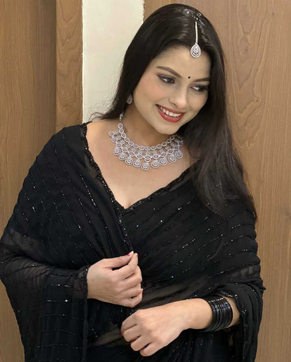 Woman wearing a black saree with silver jewelry against a wooden door background
