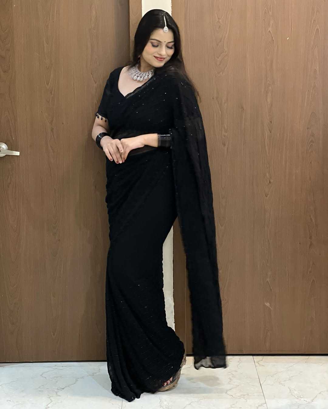 Woman wearing a black saree with a plain background