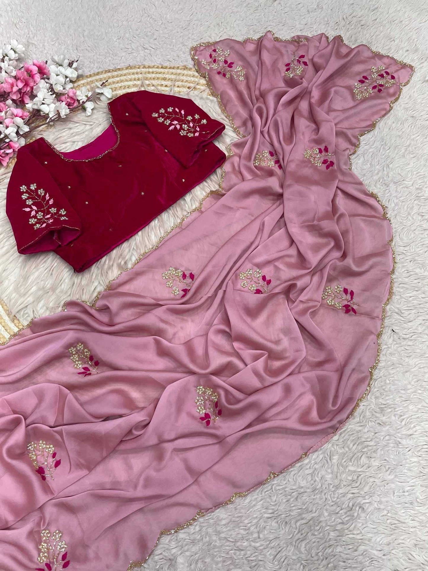 A pink georgette dupatta with gold and pink floral embroidery draped over a deep red velvet kurta, displayed on a white textured rug with decorative flowers.