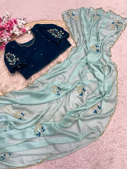 Navy blue blouse with floral embroidery on a light blue saree with similar design, on a pink background.