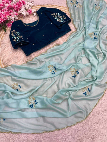 Navy blue blouse with floral embroidery on a light blue saree with similar embroidery, on a pink fabric background.
