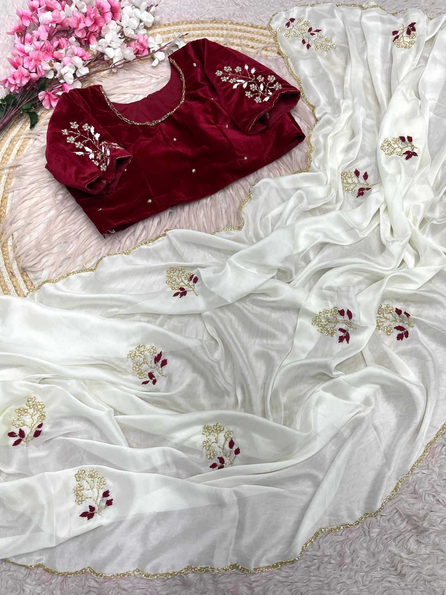 Maroon blouse with white saree featuring floral embroidery on a textured surface.