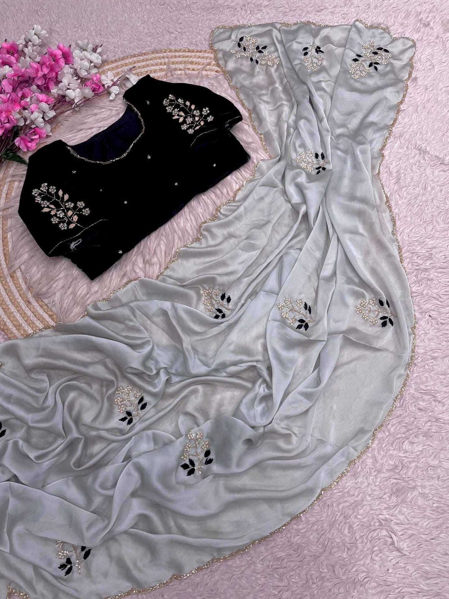 Gray saree with floral embroidery on a pink textured surface with flowers.