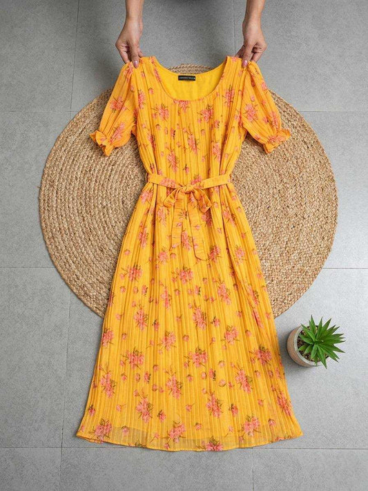 A yellow midi dress with a pink floral print, held up by a person's hands over a round woven jute mat on a gray tiled floor.