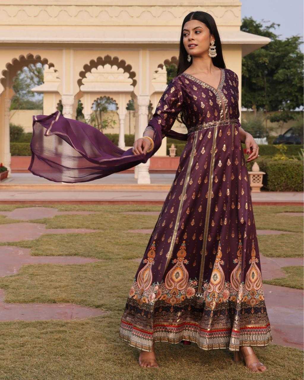 Woman in a traditional purple dress with intricate patterns standing in a garden.