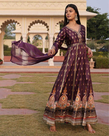 Woman in a traditional purple dress with intricate patterns standing in a garden.