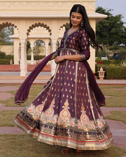 Woman in a traditional purple embroidered dress standing outdoors with a decorative archway in the background.