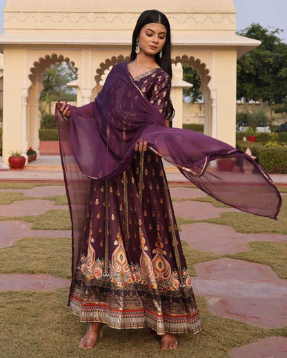 Woman in a traditional outfit with a purple dupatta standing in an outdoor setting.
