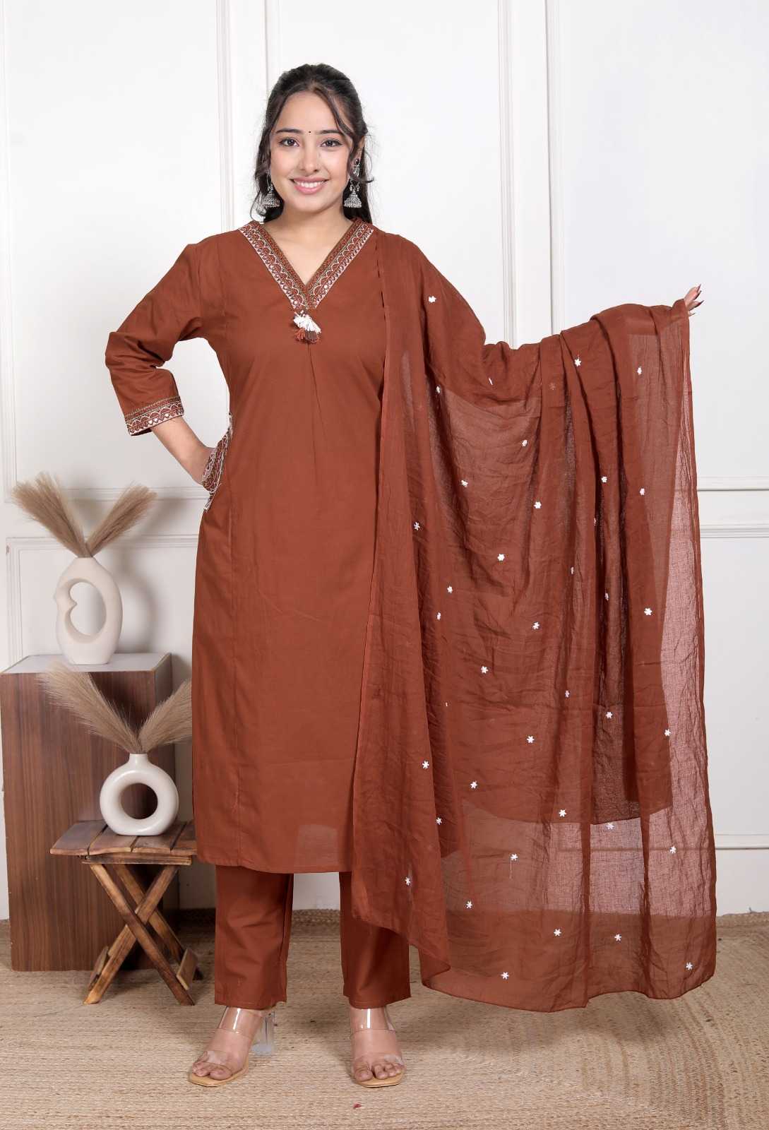 Woman wearing a brown traditional outfit with a matching dupatta, standing indoors.